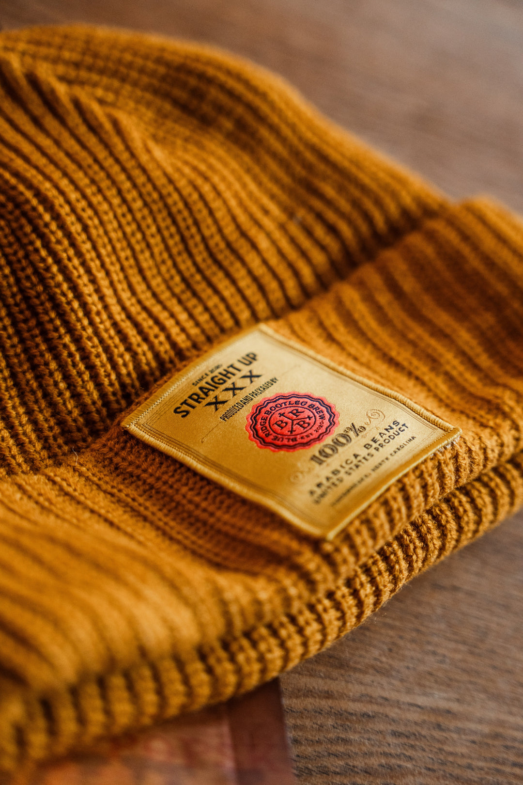 Mustard yellow beanie with a brand label on a wooden surface
